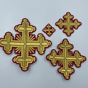 Στην φωτογραφία φαίνεται ένα Σετ κεντημένων σταυρών που αποτελείται από τέσσερεις χρυσούς σταυρούς διαφόρων μεγεθών σε κόκκινη βάση.