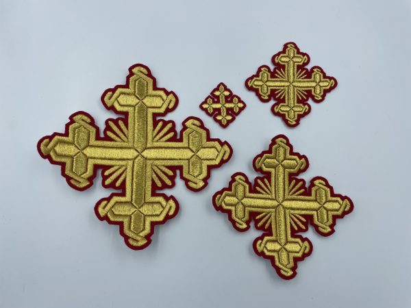 На фотографии изображен набор вышитых крестов, состоящий из четырех золотых крестов разного размера на красной основе.