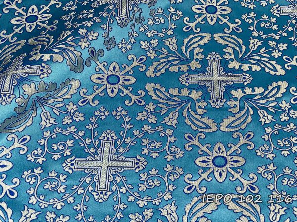 Ткань на светло-голубой основе, с крестами, ветвями и цветами серебристого цвета с голубыми деталями.