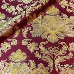 Fabric with burgundy base and gold/yellow patterns. The design is a large pine cone with leaves underneath, which is repeated.