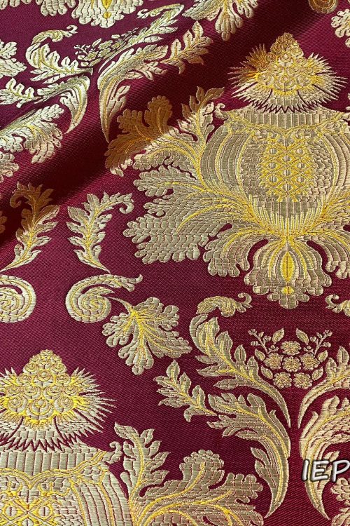 Fabric with burgundy base and gold/yellow patterns. The design is a large pine cone with leaves underneath, which is repeated.