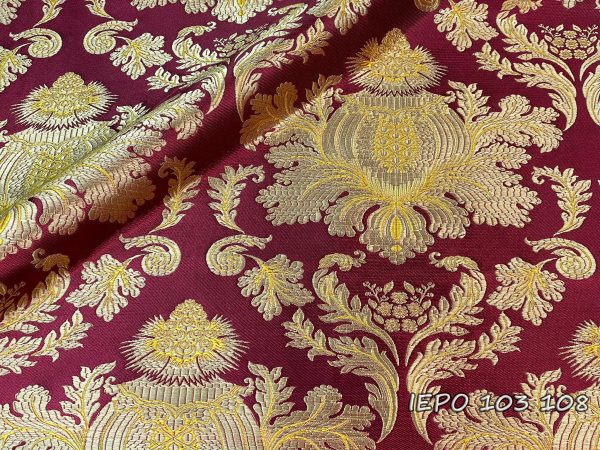 Ткань с Бургундия основой и золотисто-желтыми узорами. Дизайн представляет собой большую сосновую шишку с листьями под ней, которая повторяется.